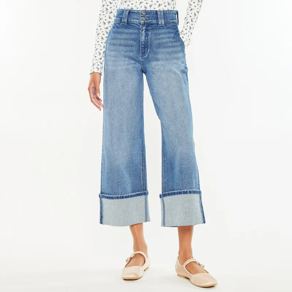 Woman wearing high-waisted, wide-leg cropped blue jeans with large folded cuffs and beige Mary Jane flats.