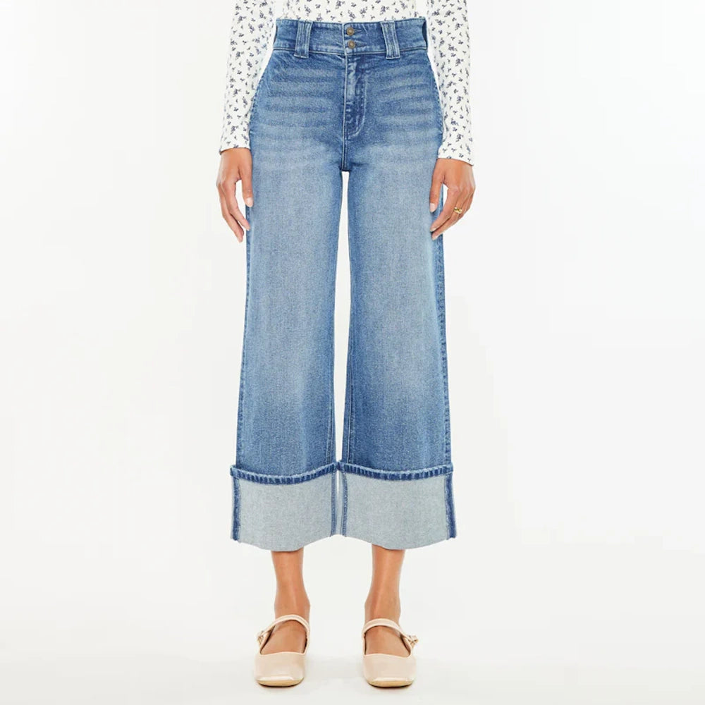 Front view of a woman wearing high-waisted cropped wide-leg jeans with wide folded cuffs and beige flats.