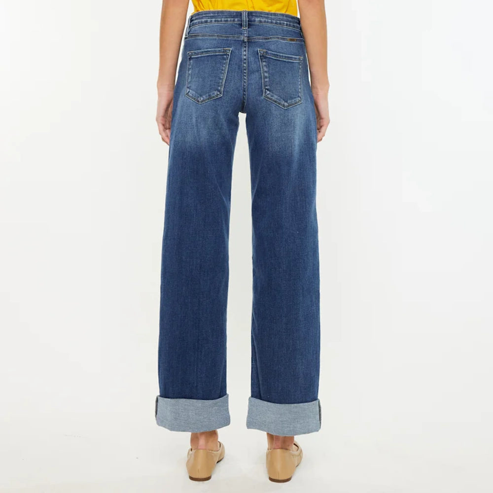 Rear view of dark wash high-rise wide-leg jeans with large cuffed hems, tan ballet flats, and a yellow shirt.