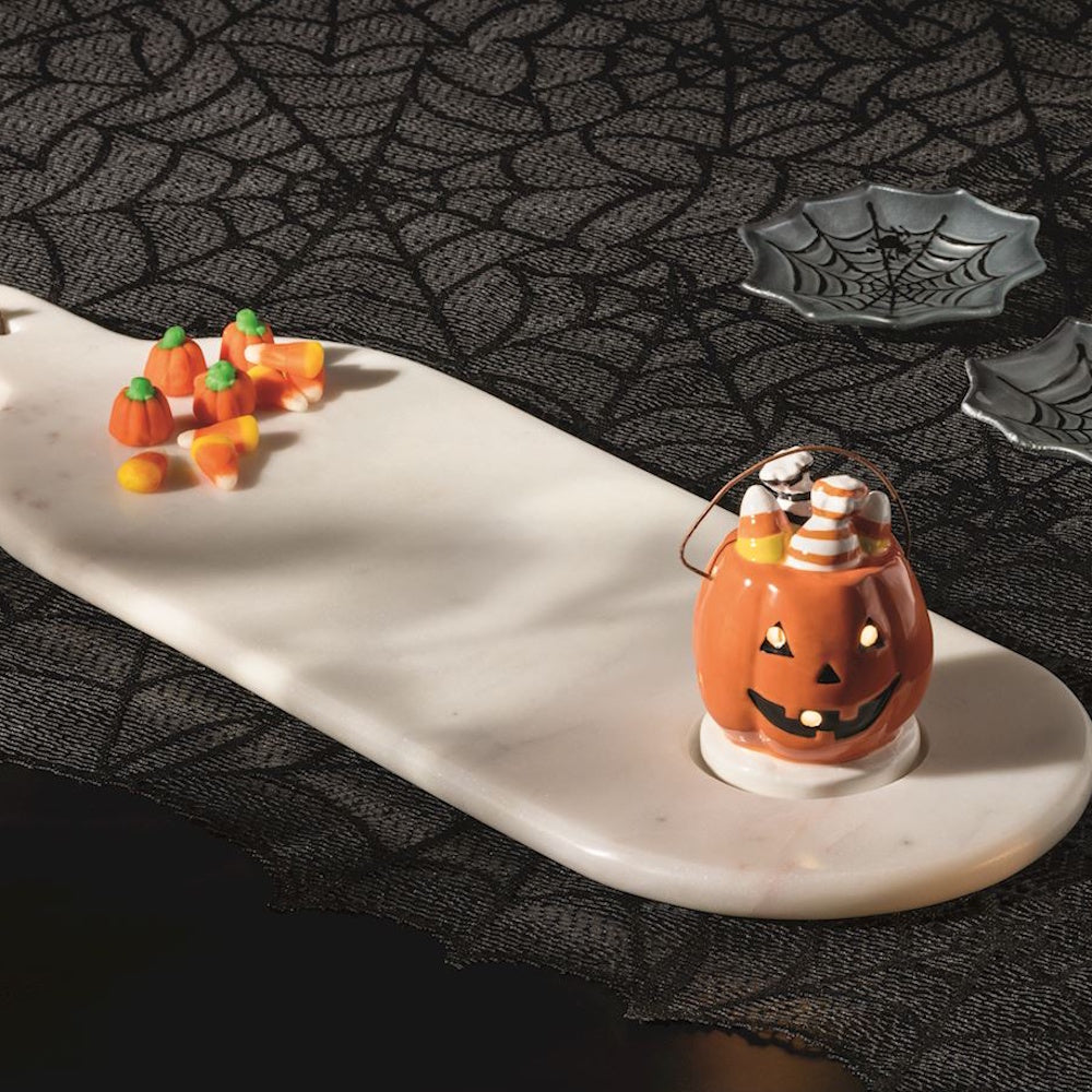 Ceramic light-up jack-o'-lantern basket on a white marble serving board with Halloween candy.