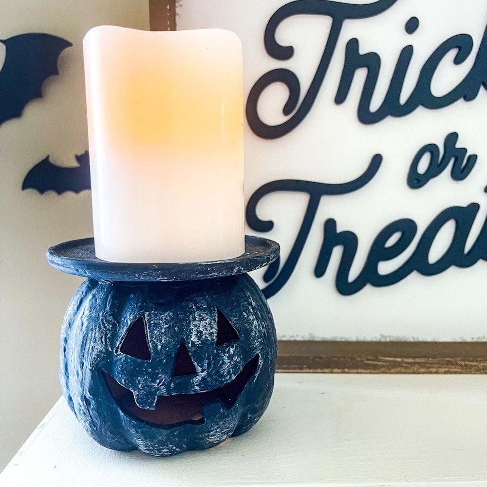 Black jack-o'-lantern candle holder with a glowing white pillar candle on top.