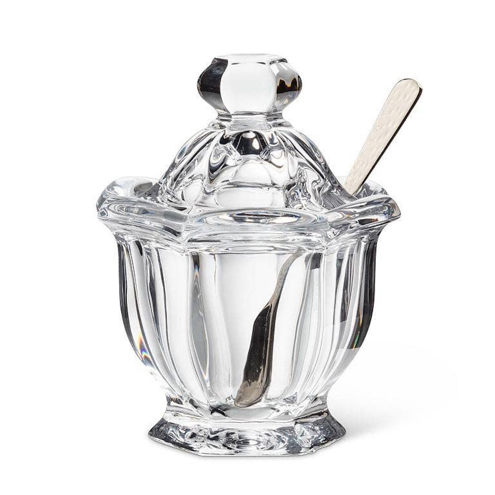 Clear glass jam jar with a matching knobbed lid and a small spoon resting inside on a white background.