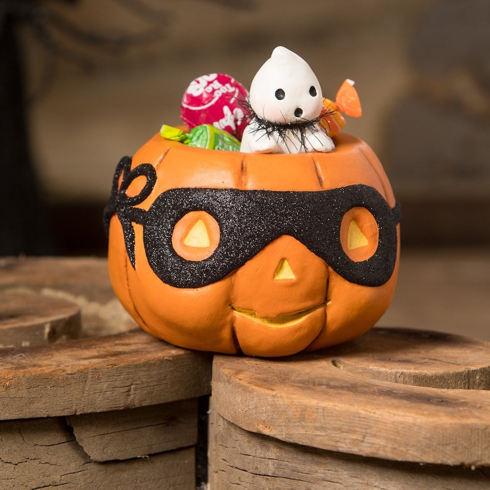 Small jack-o'-lantern dish wearing a black glitter mask, filled with candies and a cute ghost figurine.