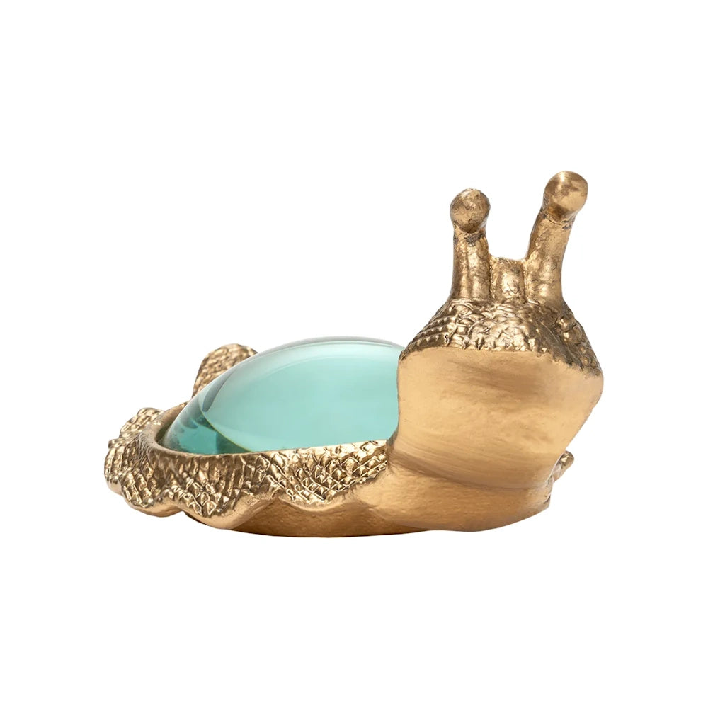 Front-facing view of a brass snail figurine with a round glass magnifying lens shell on a white background.