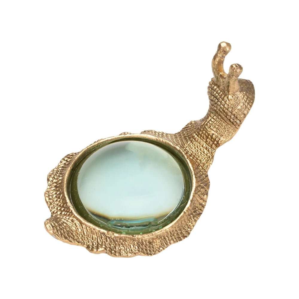 Top-down view of a textured gold snail sculpture featuring a round magnifying glass embedded as its shell.