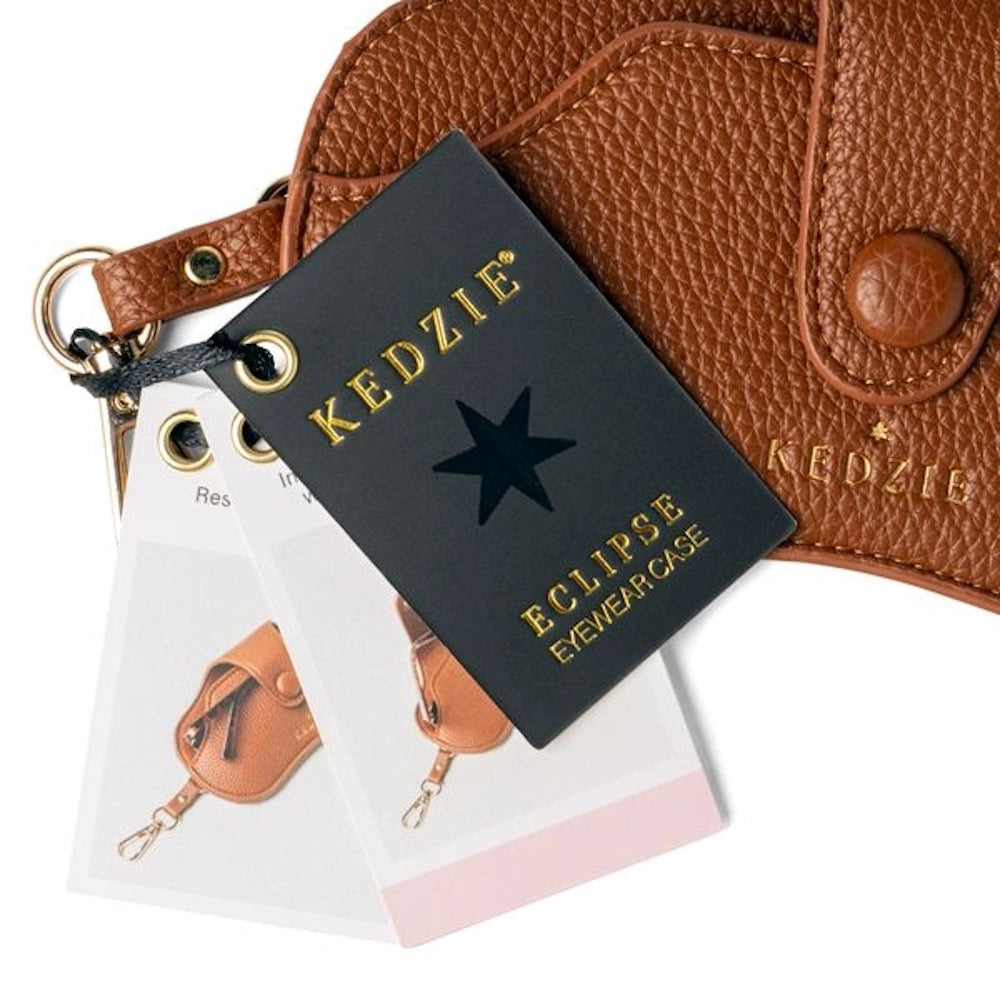 Kedzie Eclipse brown pebble leather eyewear case with gold-stamped logo, black brand tag, and product information cards.
