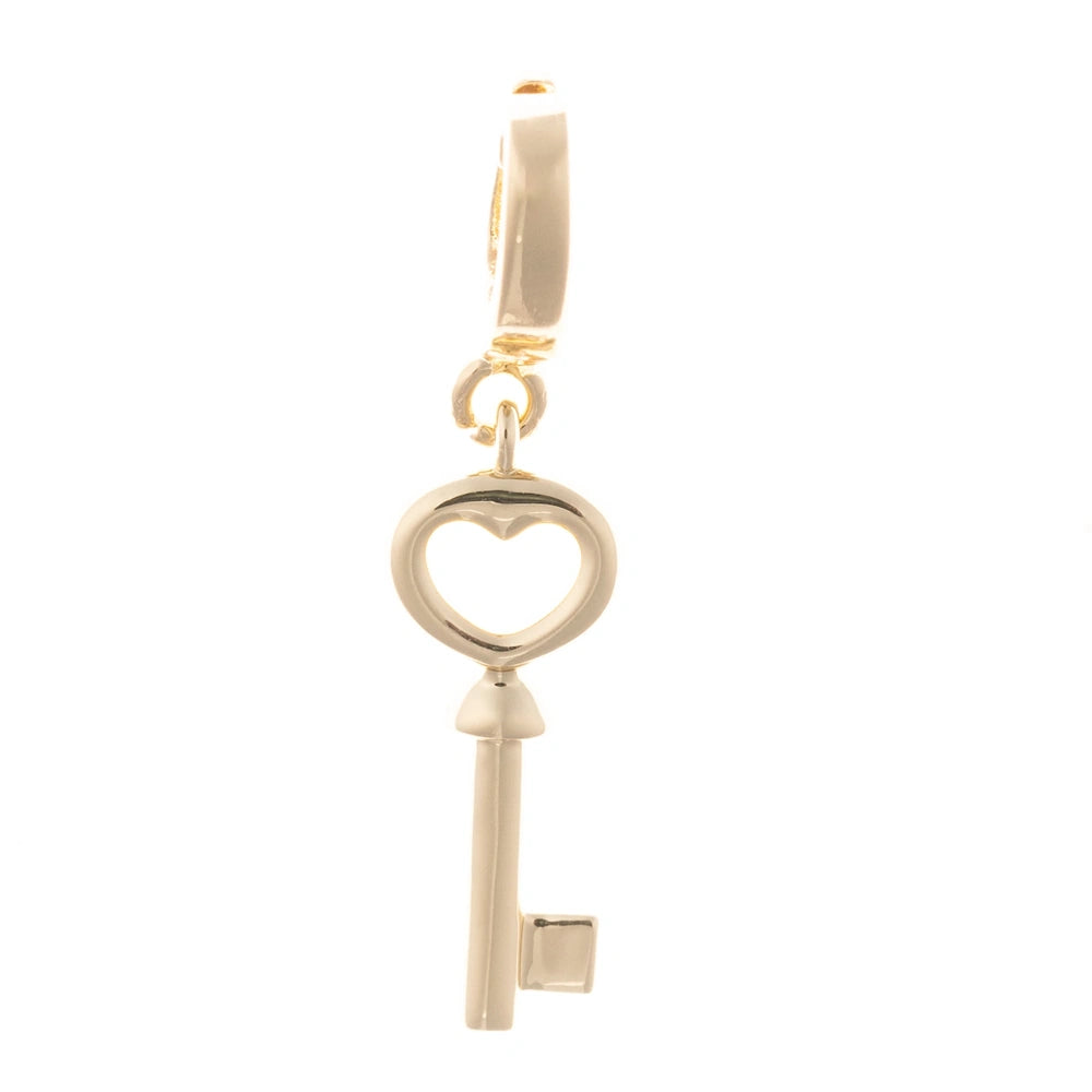 Polished gold key charm featuring a heart-shaped bow, set against a plain white background.