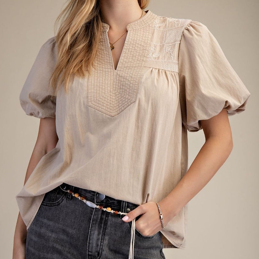 Beige puff sleeve blouse with embroidered yoke and V-neckline paired with dark grey jeans.