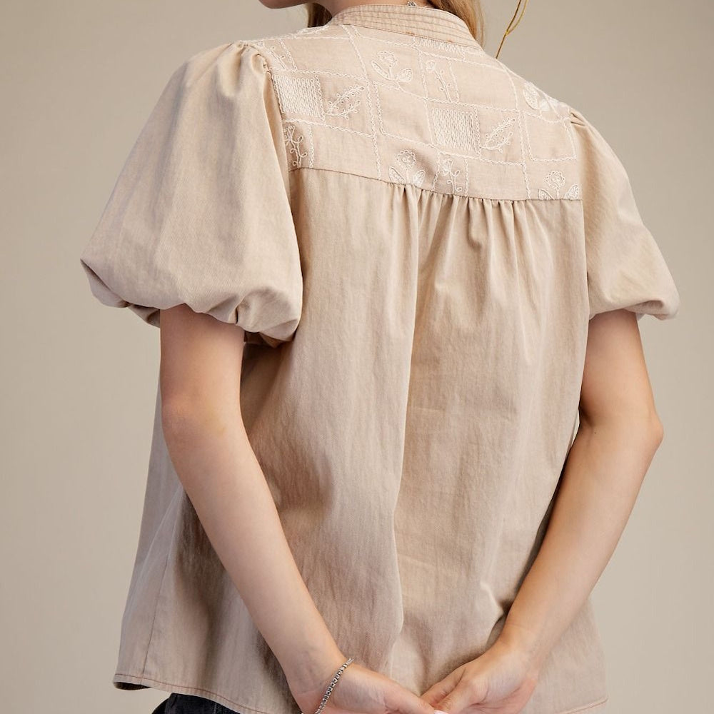Woman wearing a neutral boho top with short puff sleeves and embroidered back panel.