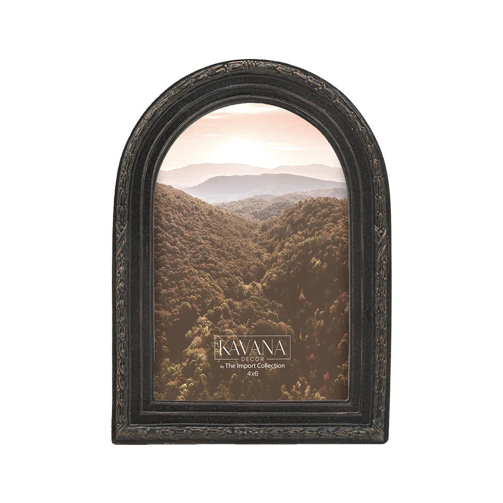An arched black picture frame with ornate details, displaying a photo of a forested mountain landscape.