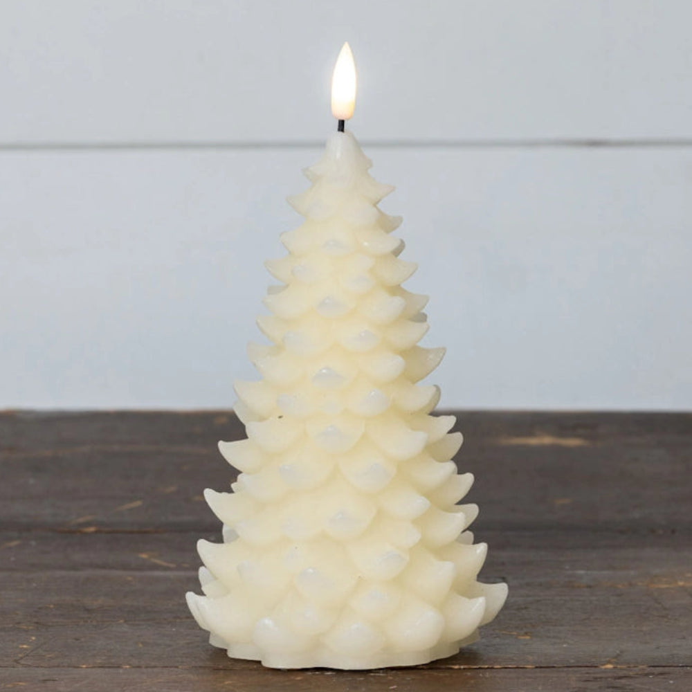 Lit flameless cream candle shaped like an evergreen tree, resting on a wooden surface.