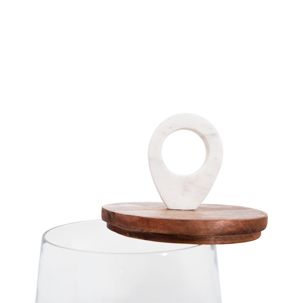 An open glass jar with a wooden lid featuring a white marble loop handle sitting on the rim.