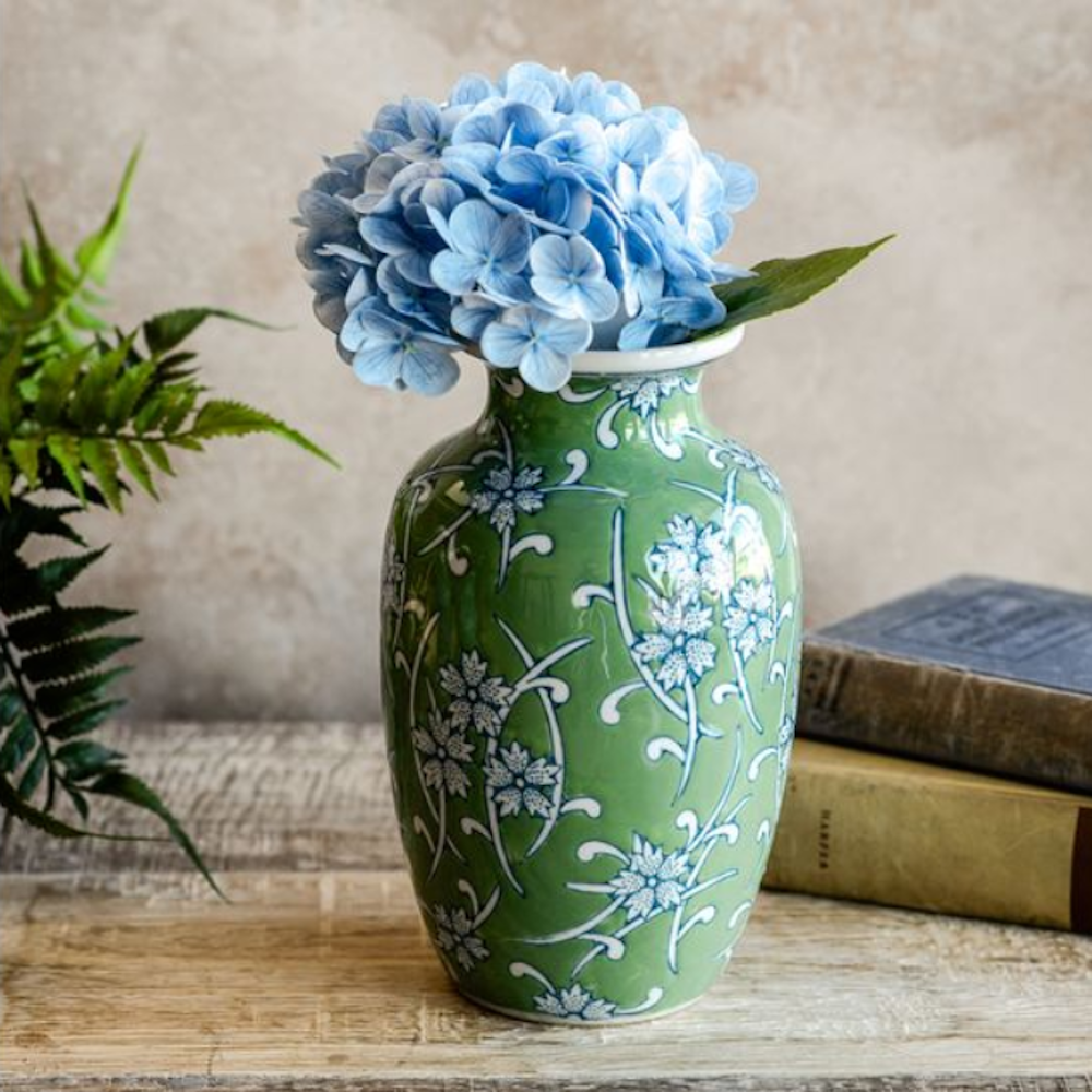 Green ceramic vase with blue floral patterns holding a bunch of light blue hydrangeas.