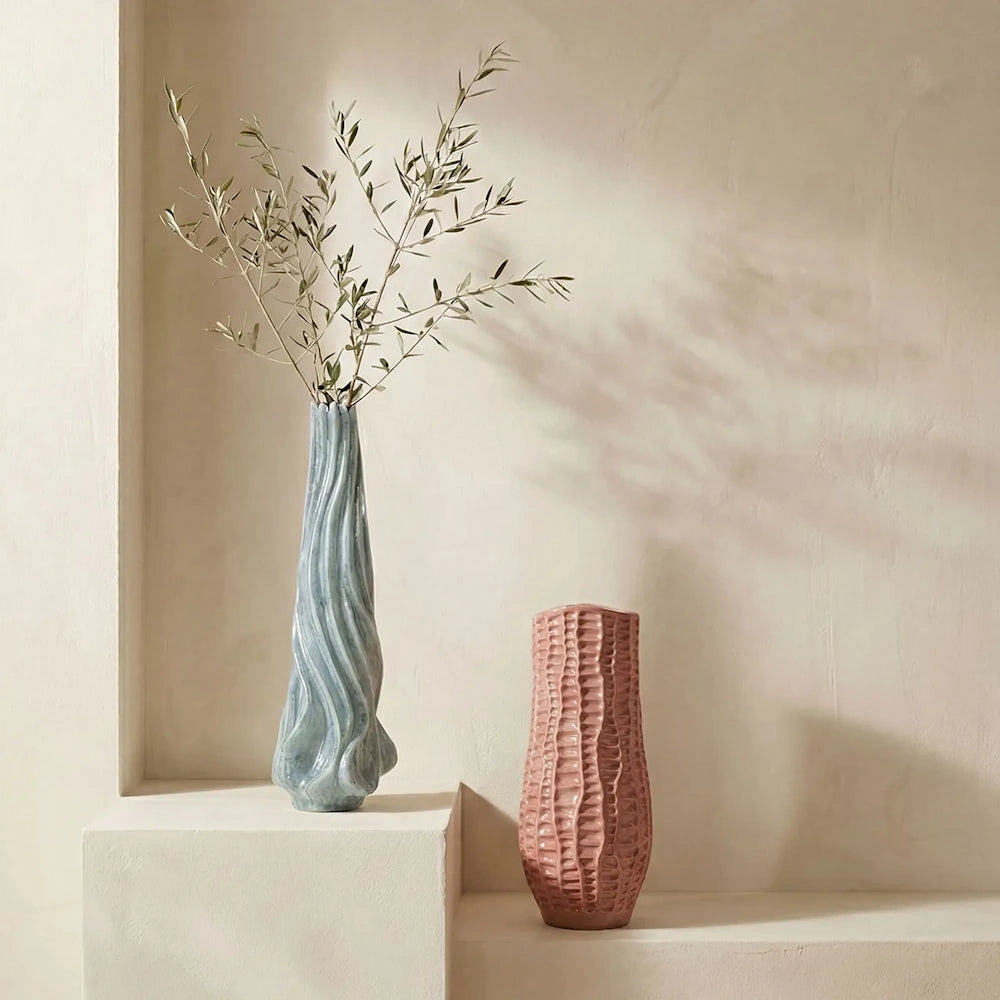 Two ceramic vases, one tall light blue with wavy ridges and branches, and one shorter textured dusty pink.