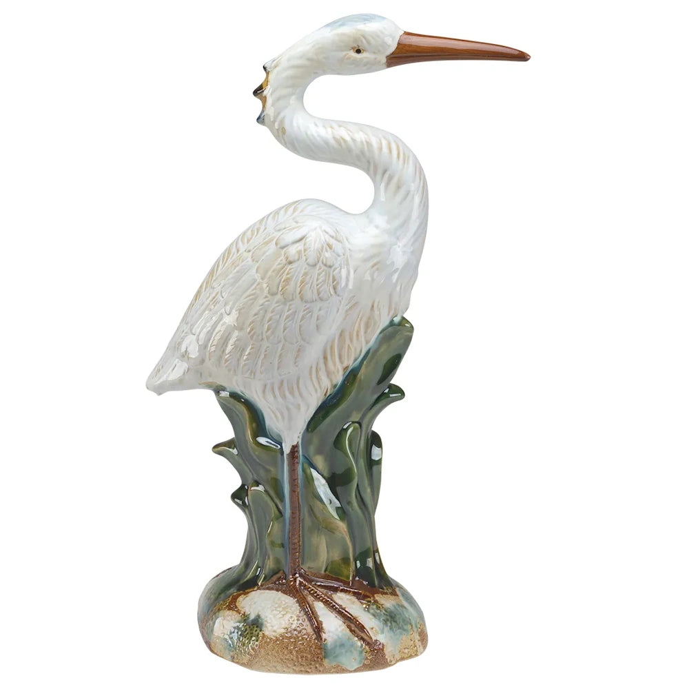 White ceramic heron figurine with a long brown beak, standing on a green and beige base.