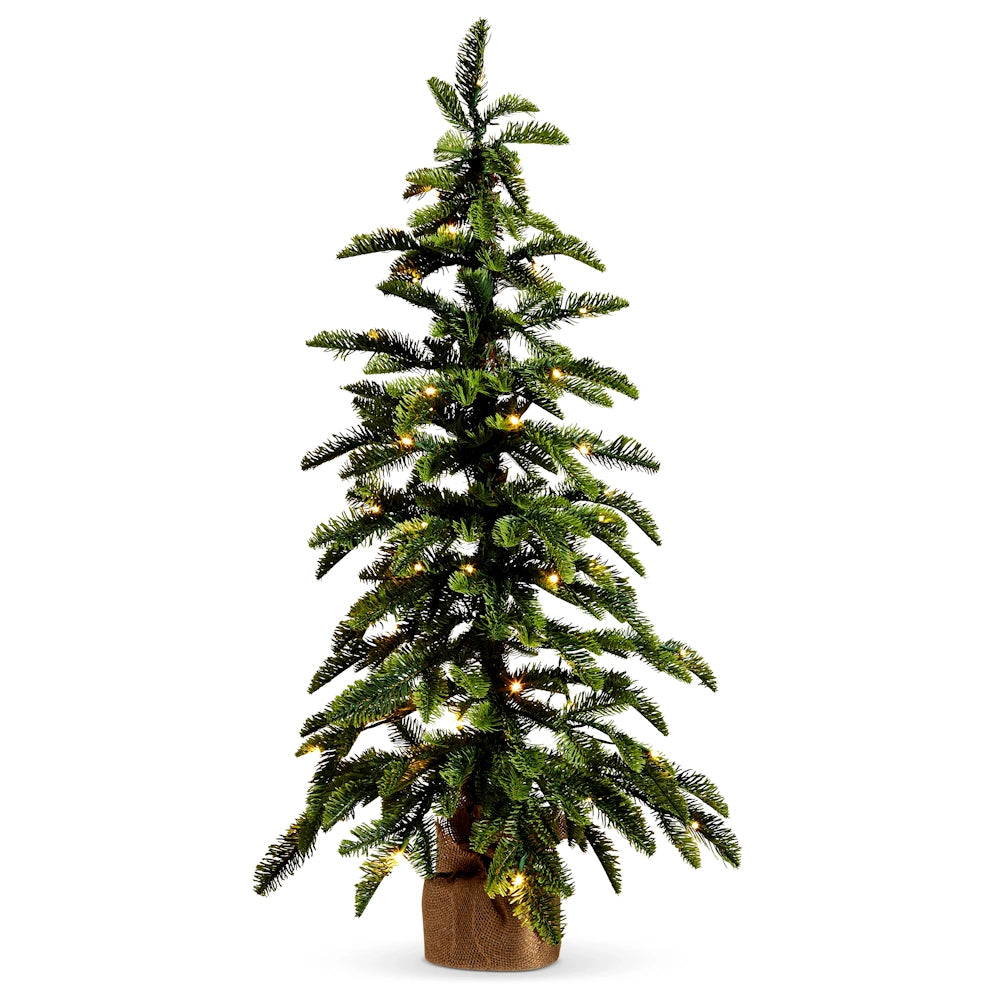 Tall artificial pine tree decorated with warm white lights and set in a burlap base.