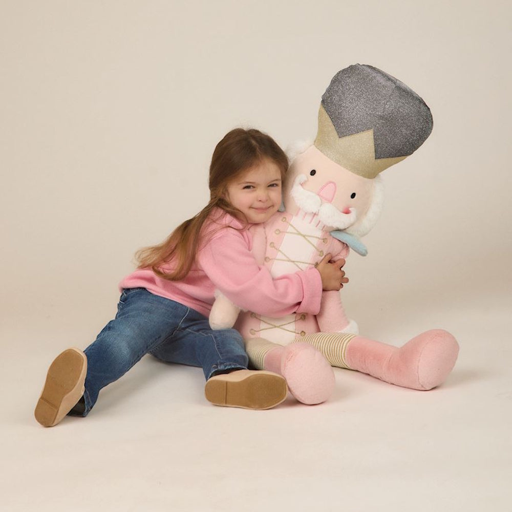 Young girl in a pink sweater hugging a large plush pink nutcracker doll.