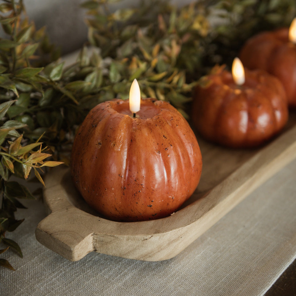 Orange pumpkin-shaped flameless LED candles arranged in a wooden dough bowl with leafy garland.