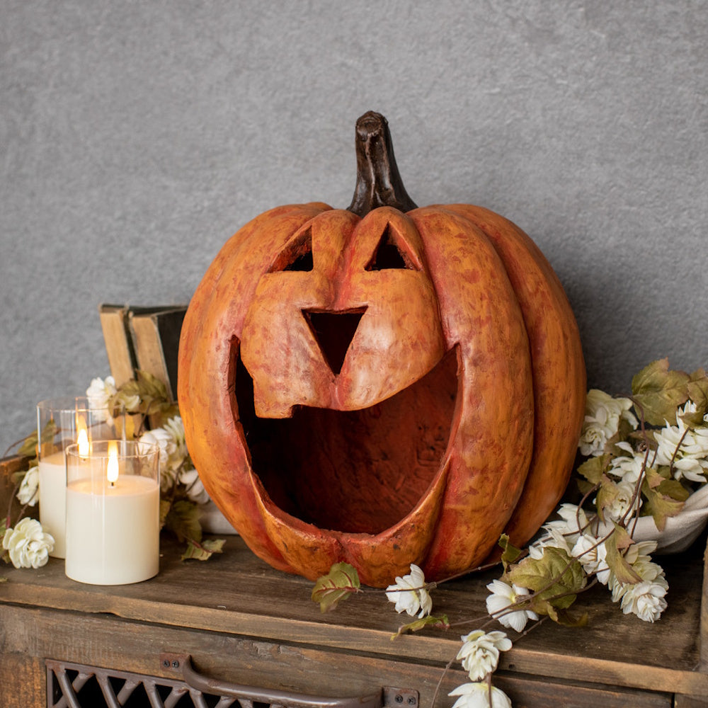 Large orange jack-o'-lantern with a open smile on a rustic wooden table beside pillar candles and florals.