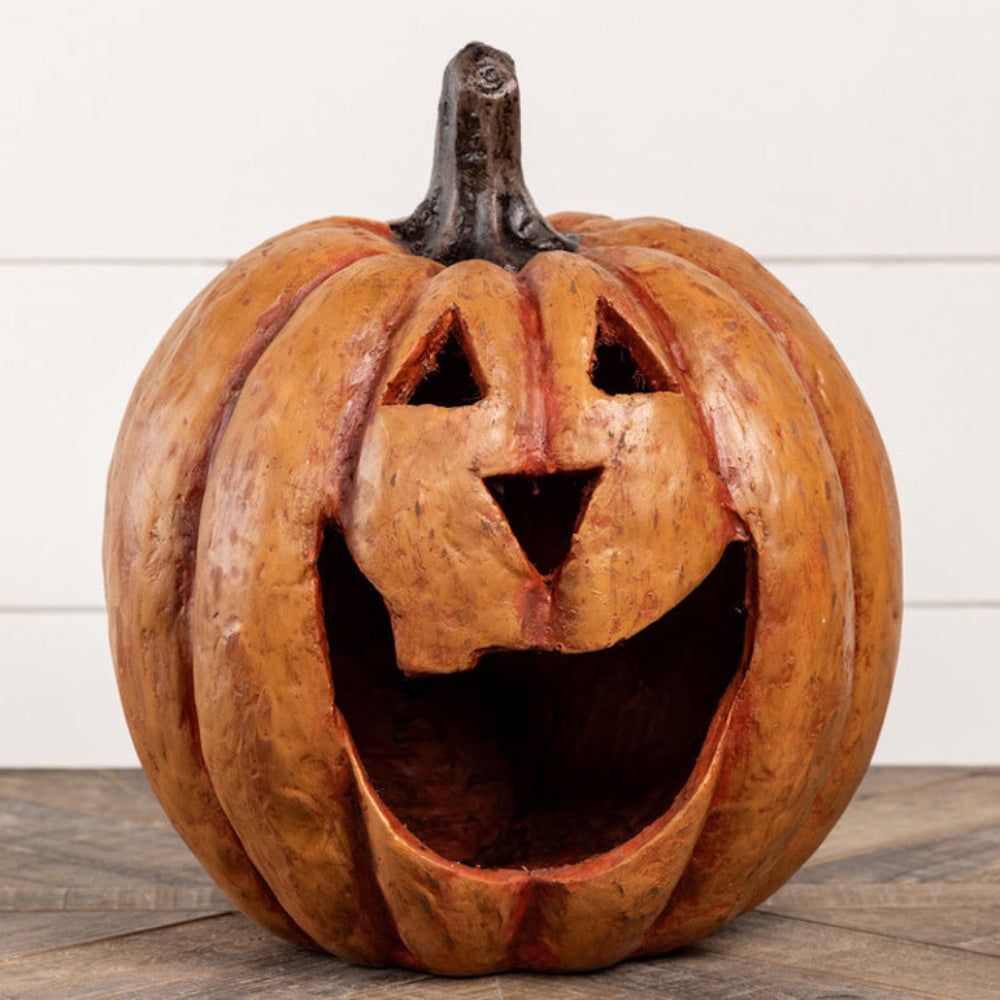 Large carved orange jack-o'-lantern resting on a wooden surface against a white wall.