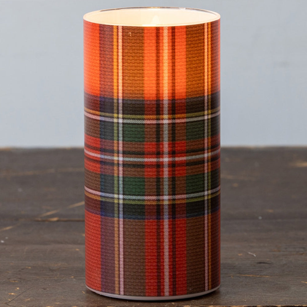 Lit flameless pillar candle with a red tartan plaid pattern on a wooden surface.