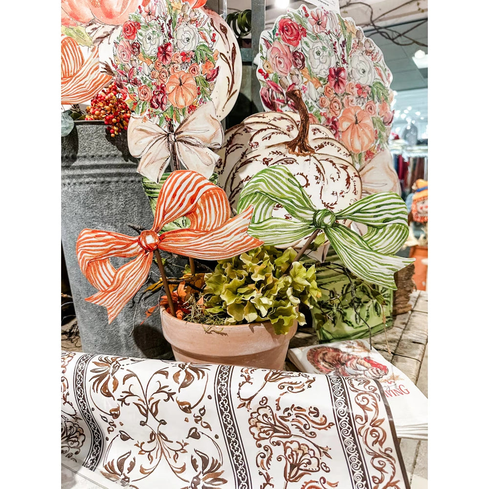 Floral pumpkin decorations in a terracotta pot with large striped bows and a patterned table runner.