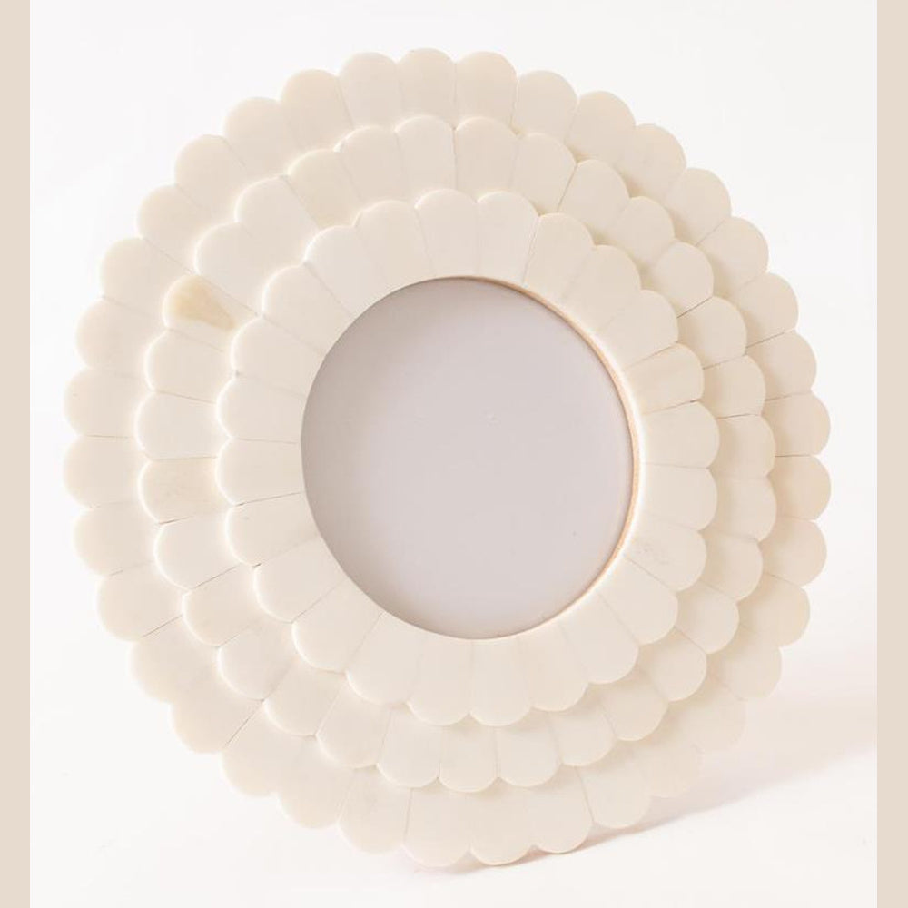 A close-up of a round white bone photo frame featuring a tiered scalloped petal design against a neutral background.