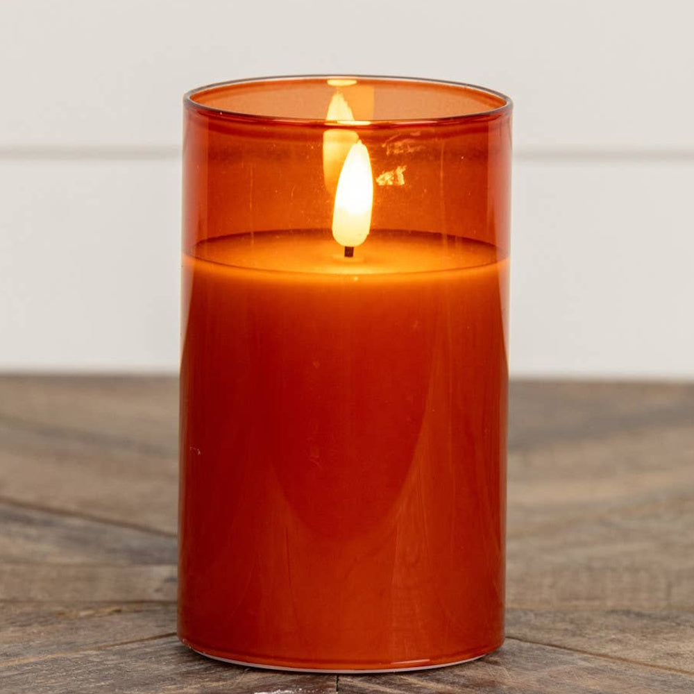 Lit sienna glass pillar candle sitting on a wooden surface.