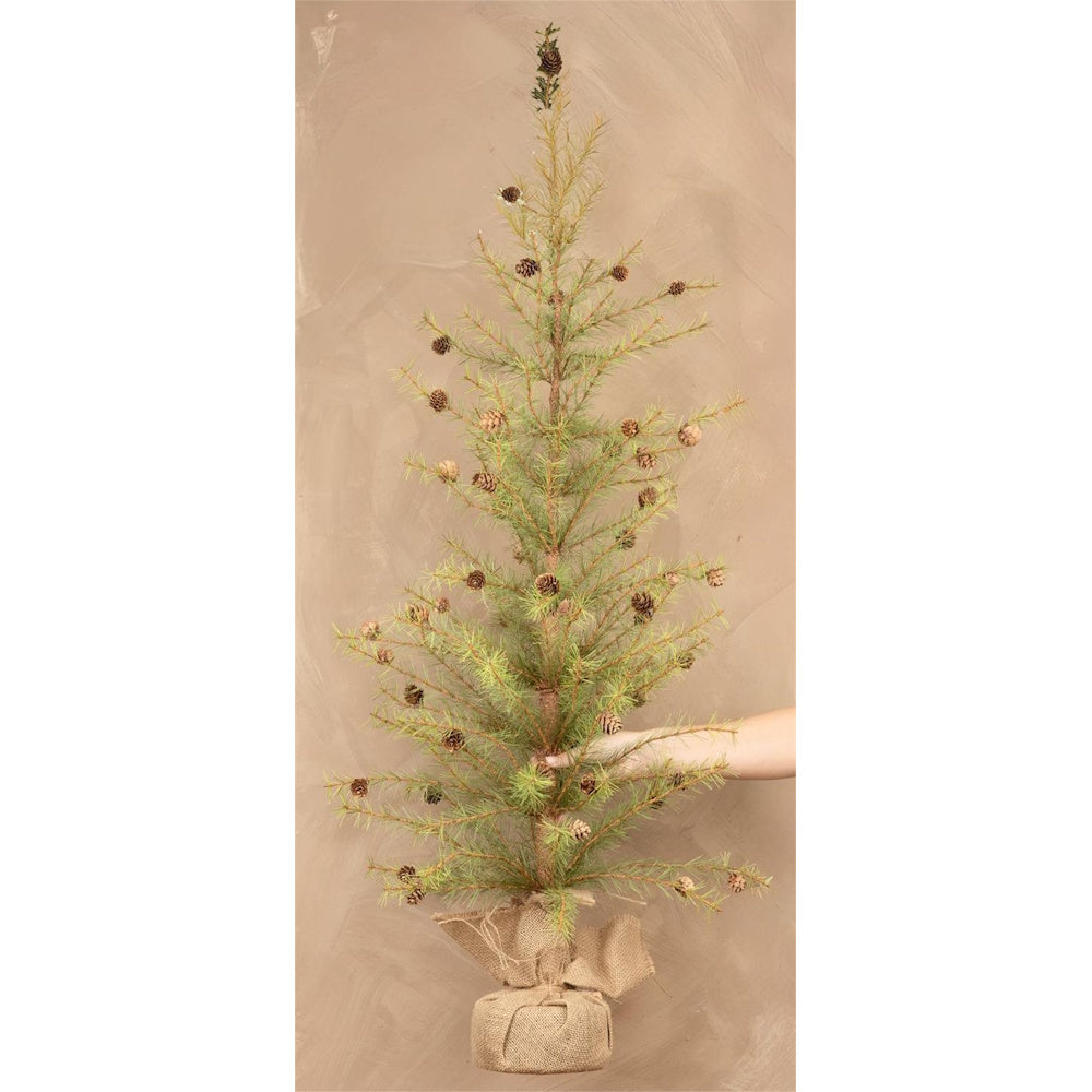 A small potted pine tree with pinecone decorations and a burlap-wrapped base held by a hand.