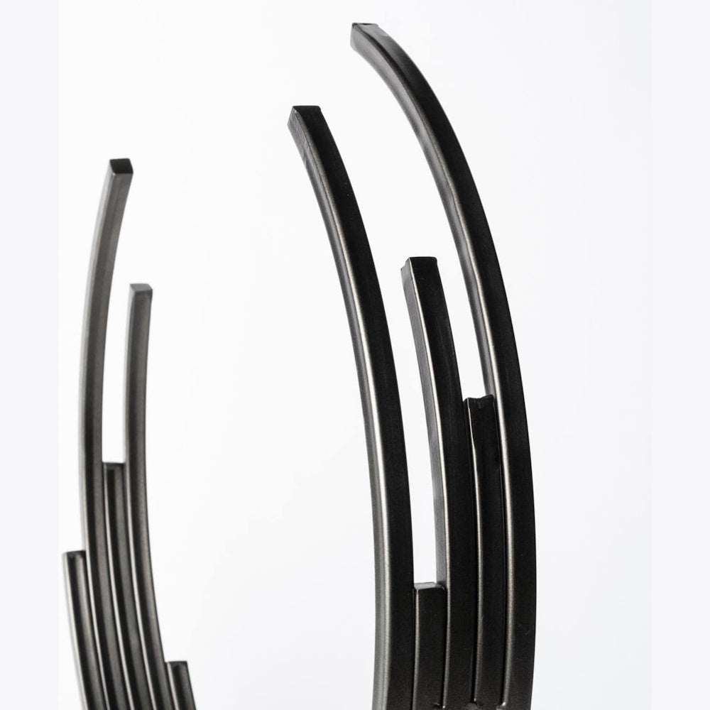 Close-up of matte black metal circular sculpture detail, showing tiered square-edged arcs against a white background.