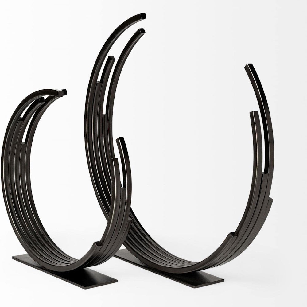 A pair of minimalist, dark bronze crescent-shaped metal art sculptures with segmented bars, standing on flat bases.
