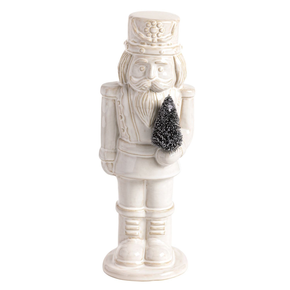 Off-white ceramic nutcracker figurine holding a miniature frosted bottle brush tree.