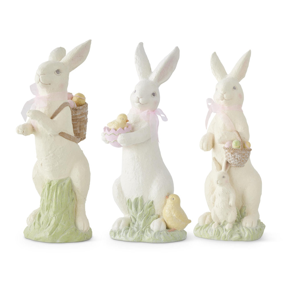 Three white resin Easter bunny figurines with pink bows, holding baskets and baby chicks on green grass bases.