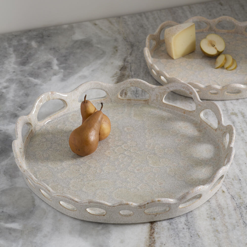 Two round, scalloped ceramic trays on marble, one with two pears and the other holding cheese and sliced apples.