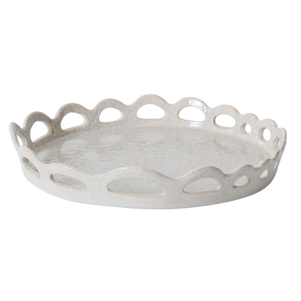 A round, speckled beige ceramic tray with a scalloped, cutout border against a white background.