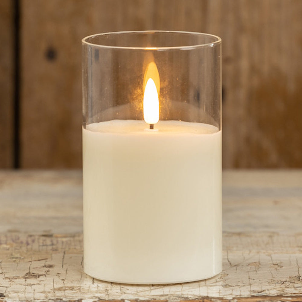 Flameless white pillar candle with a glowing flame inside a clear glass cylinder cylinder holder.