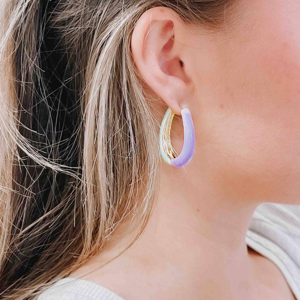 Close-up of a person's ear wearing a thick, oval hoop earring with a light purple and pastel green design.