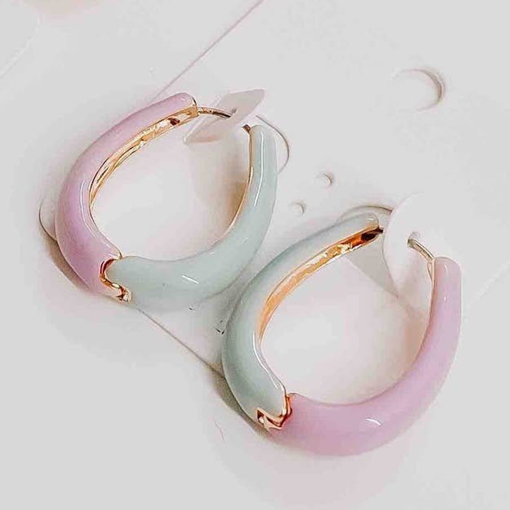 A pair of thick hoop earrings featuring a split design of pastel pink and light green enamel on gold trim.
