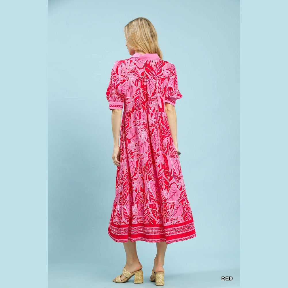 Back view of a woman in a pink and red leafy print midi dress with short puff sleeves and a patterned border hem.