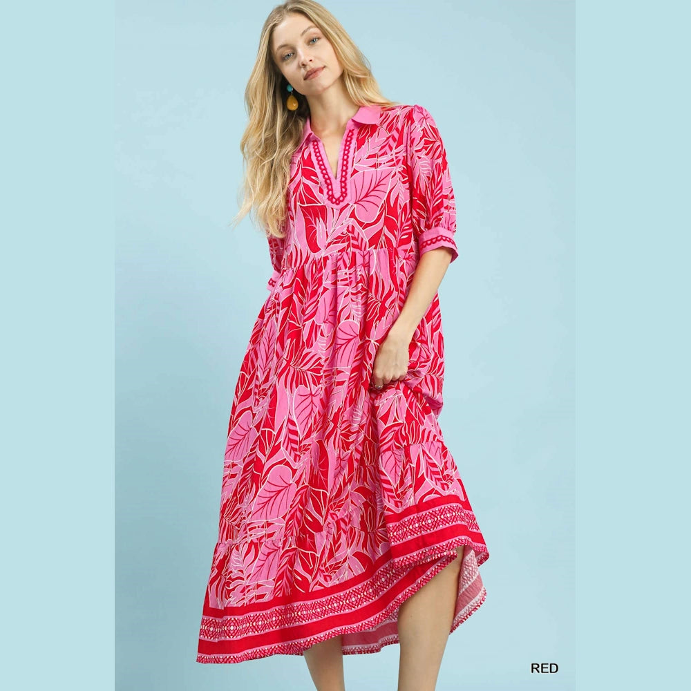 Woman wearing a red and pink leafy border print v-neck midi dress against a light blue background.