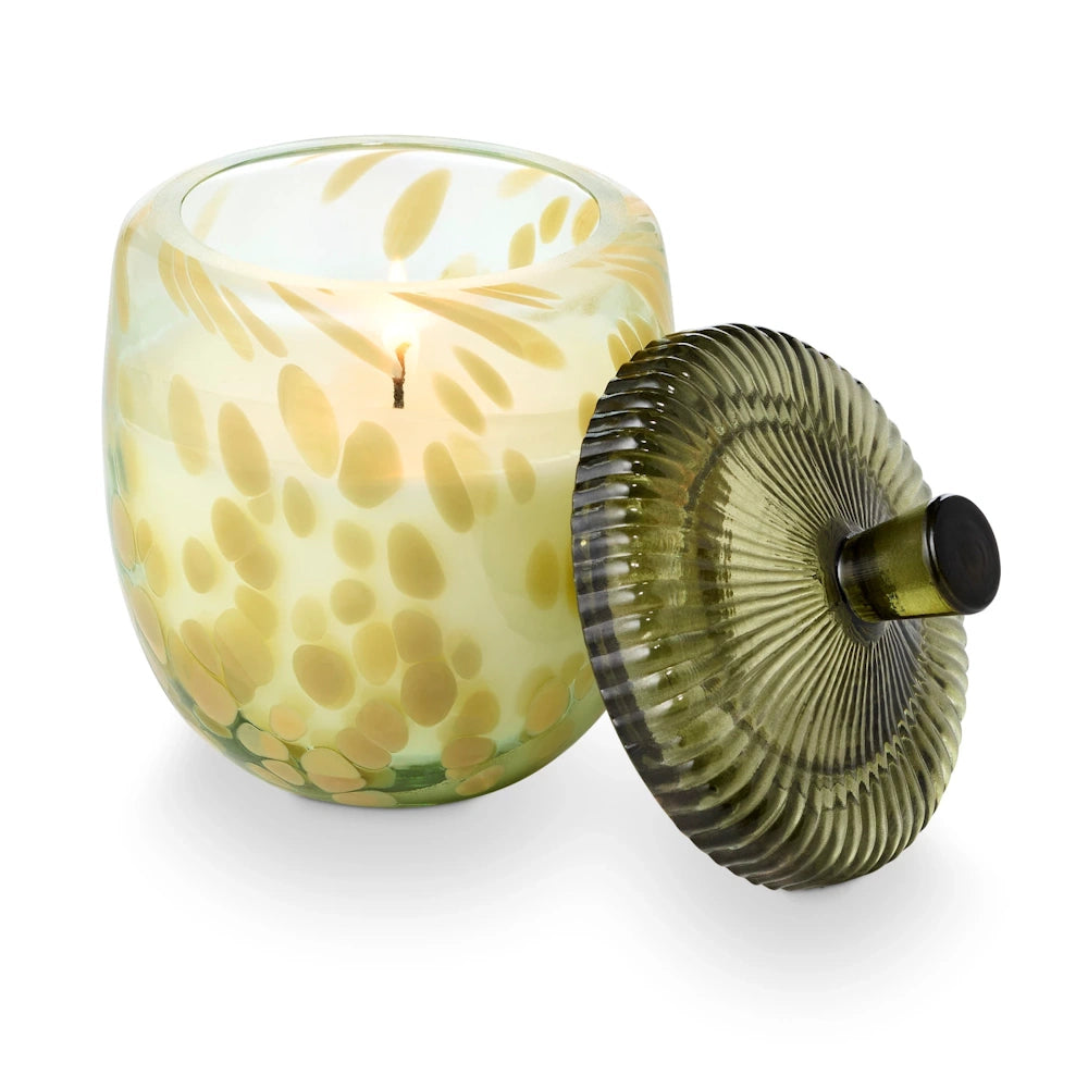 Lit speckled glass acorn candle jar with a dark green ribbed lid.