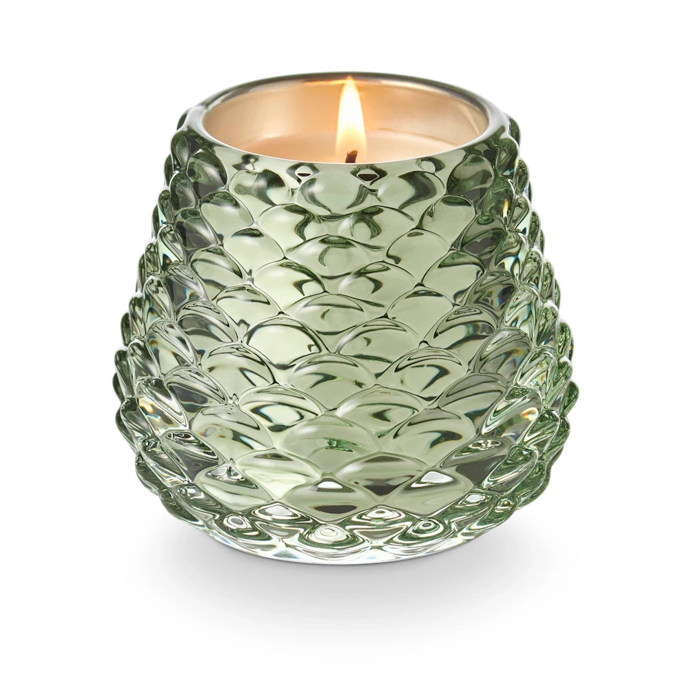 Lit scented candle in a textured sage green glass pinecone votive holder.