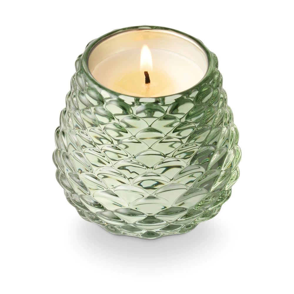 Lit textured green glass pinecone votive candle holder on a white background for seasonal decor.