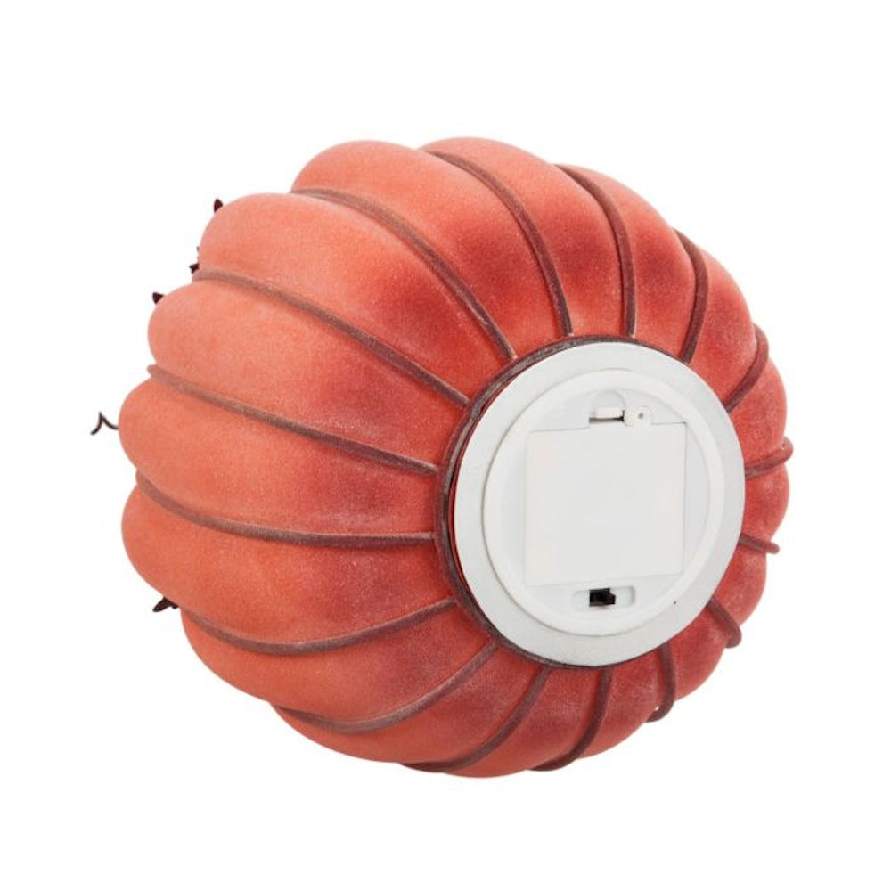 Bottom view of an orange velvet decorative pumpkin showing its battery compartment and switch.