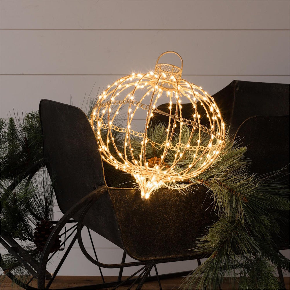 Lit wire ornament sphere glowing with warm LED lights placed inside a vintage metal sleigh.