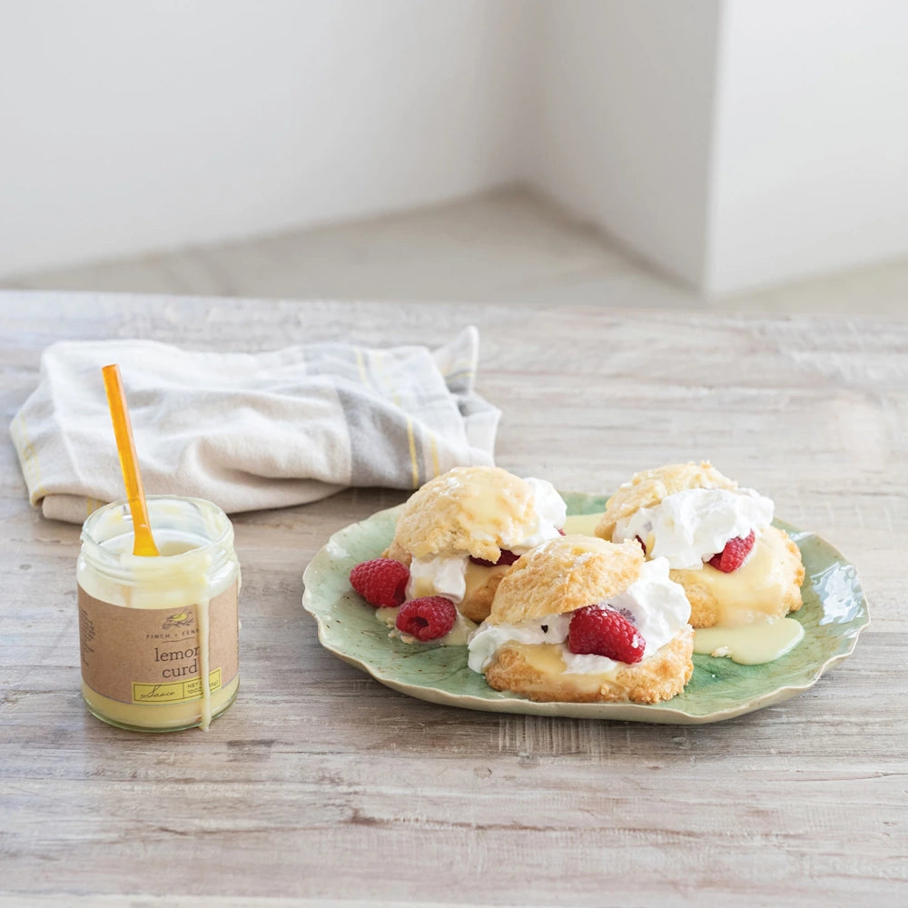 Lemon curd drizzled over cream and raspberry scones on a green plate next to a jar of Finch + Fennel lemon curd sauce.