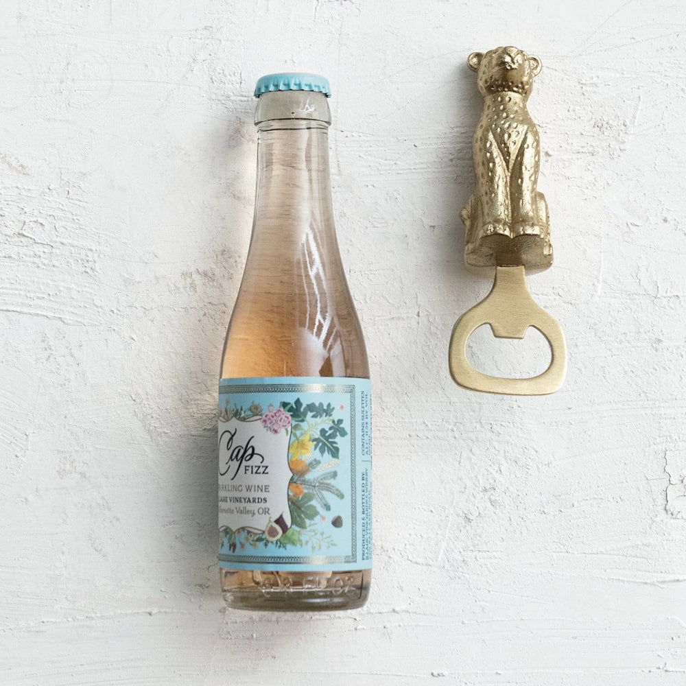 Bottle of Cap Fizz sparkling wine from Willamette Valley, OR, next to a gold cheetah-shaped bottle opener.