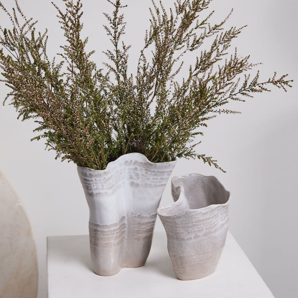 Two wavy, textured ceramic vases on a pedestal, with the taller one holding a large bouquet of dried greenery.