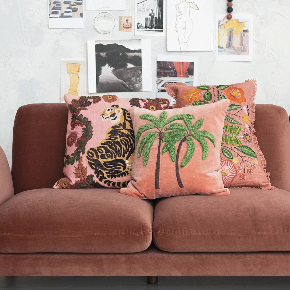 Boho chic embroidered throw pillows featuring a tiger and palm trees on a dusty rose velvet couch.