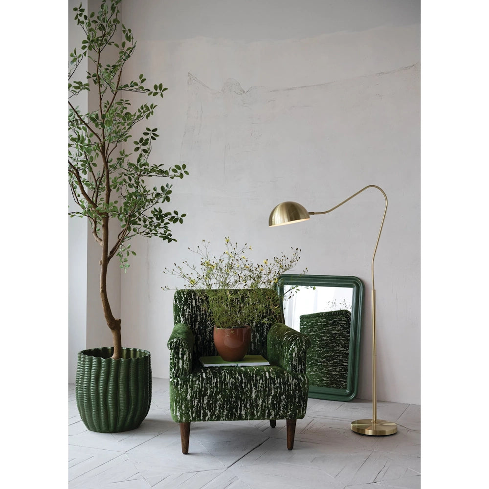 Green fluted stoneware planter with a tall indoor tree next to a patterned green velvet armchair and brass floor lamp.